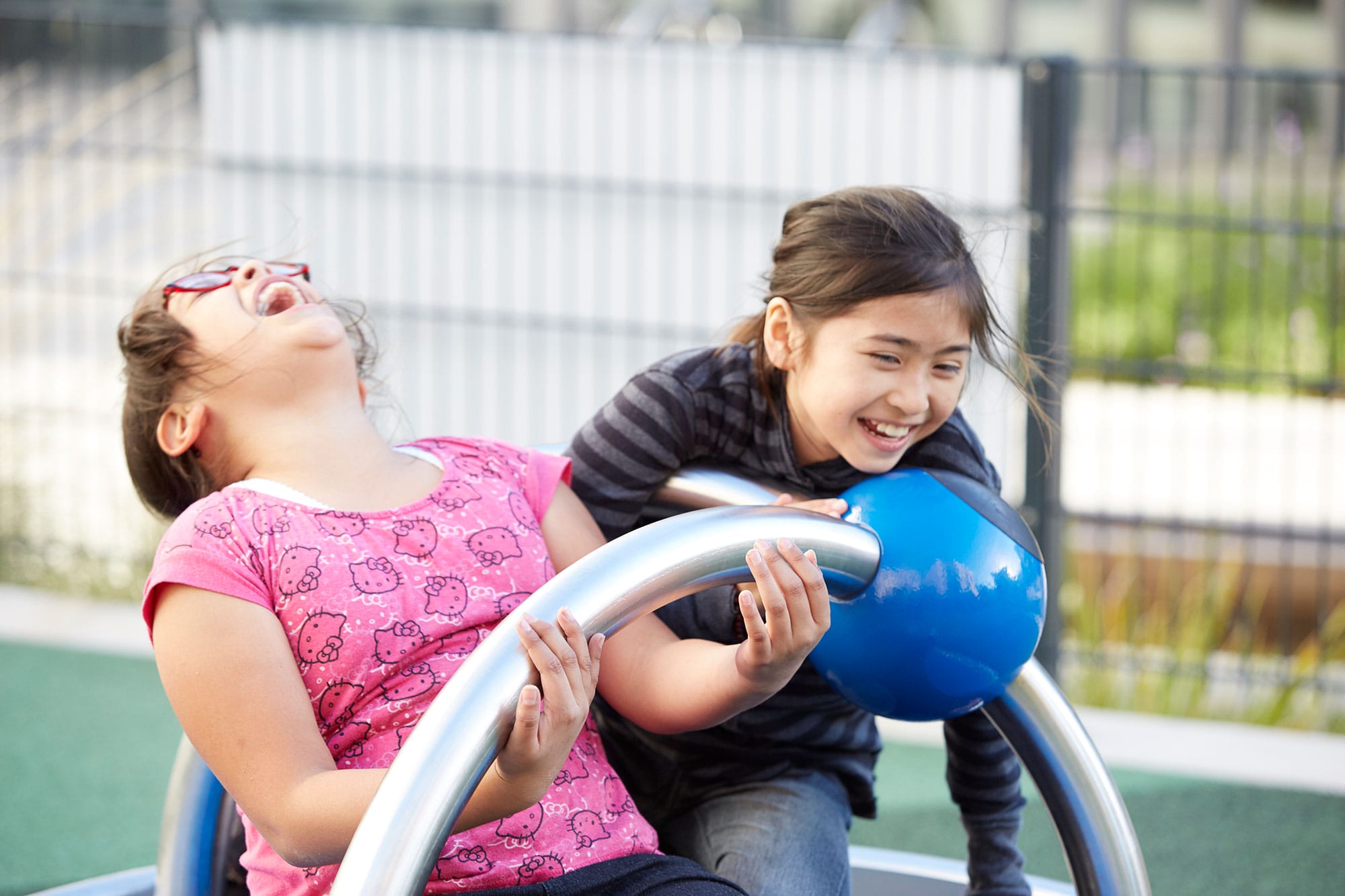 Two girls playing on a playground with a blue ball.