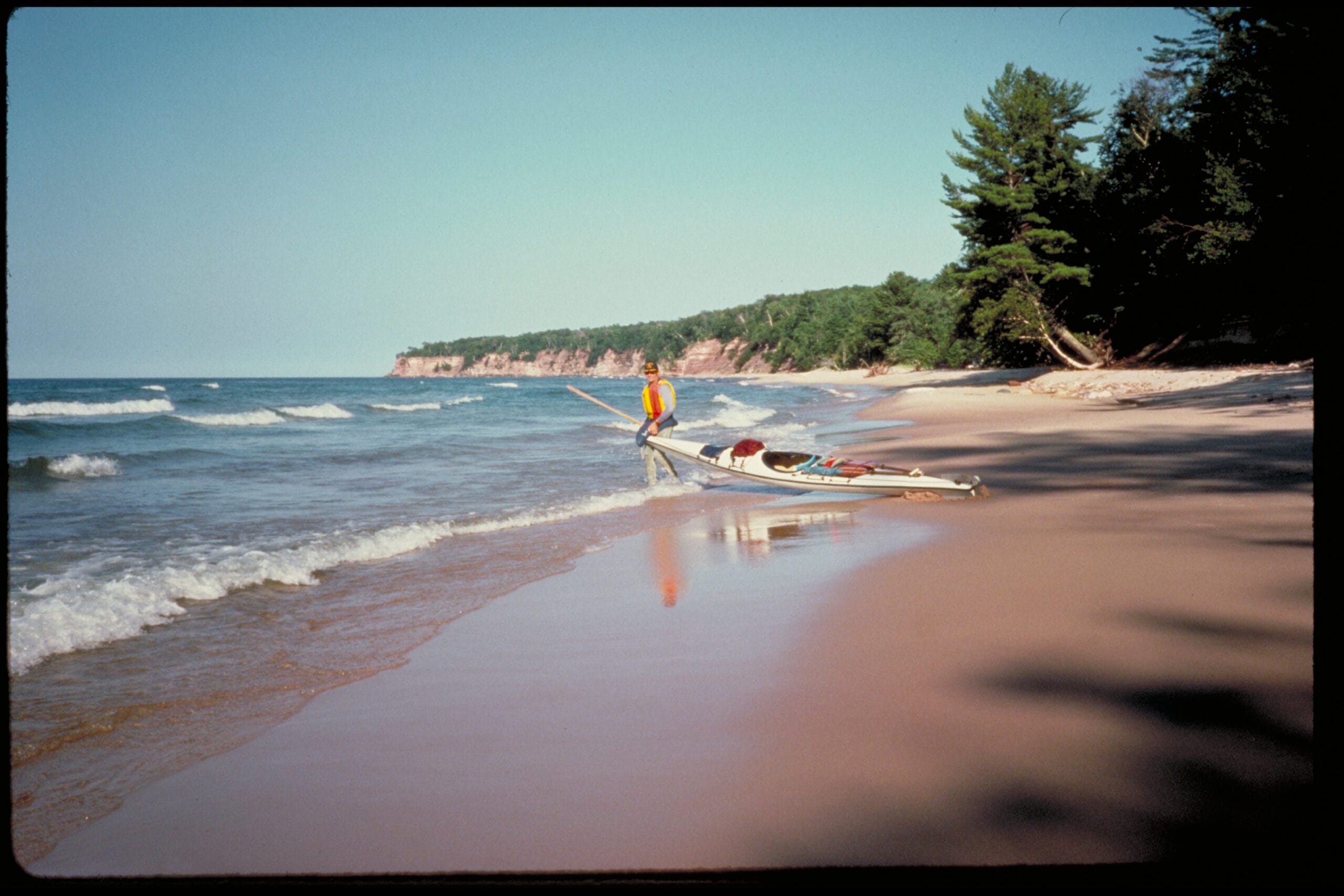 A person is paddling a canoe on a beach.