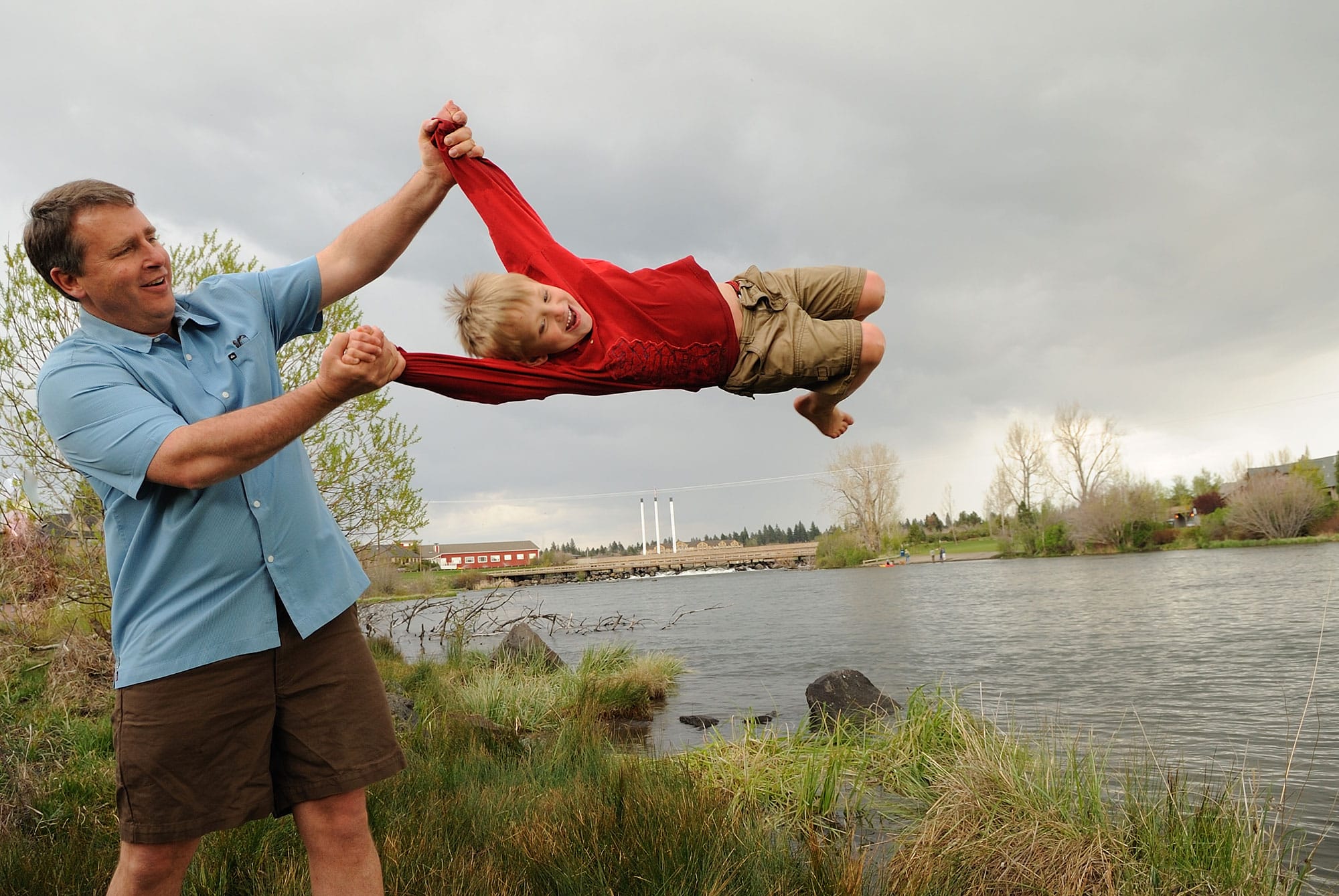 A man and a child in the air near a river.