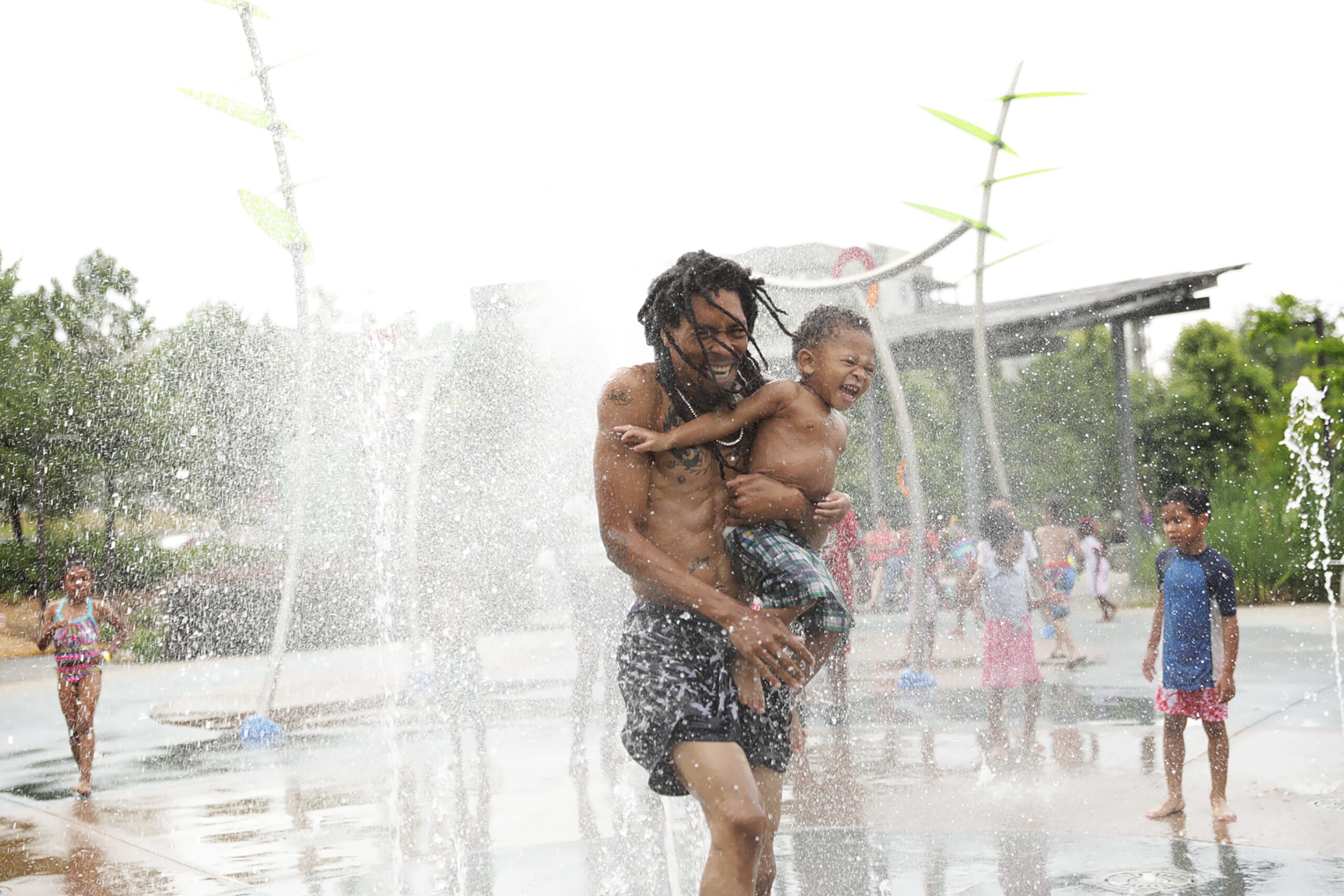 A man and a child playing in a water fountain.