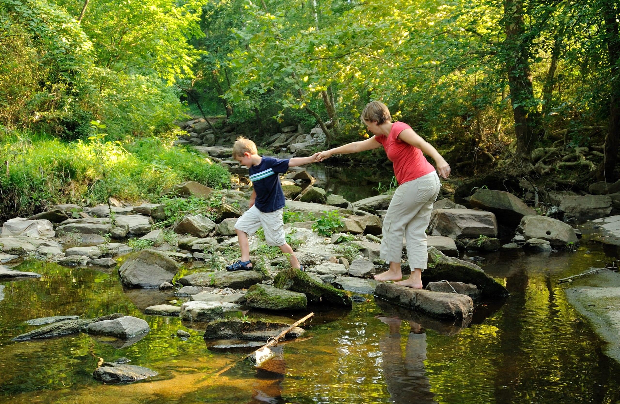 A woman and child standing on rocks in a stream.