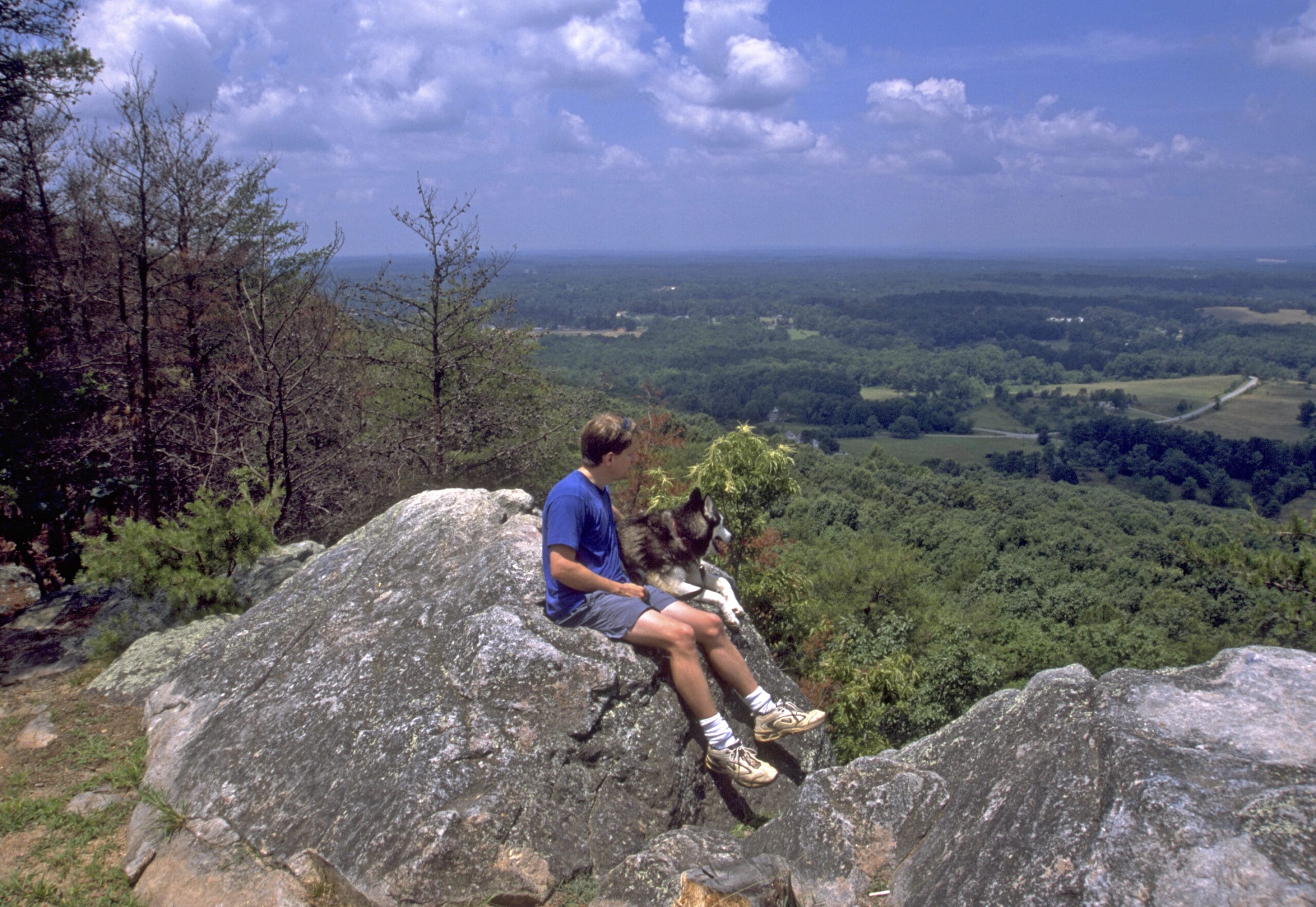 A man sitting on a rock with his dog.