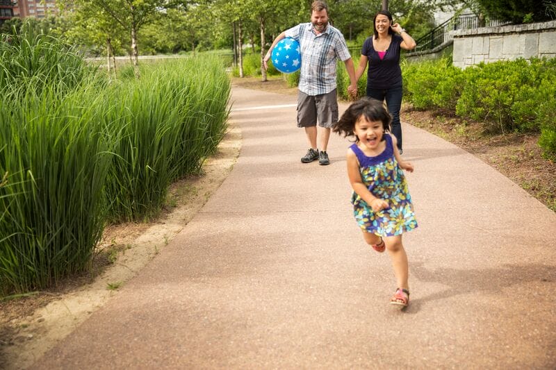 A family with a young girl running down a path.