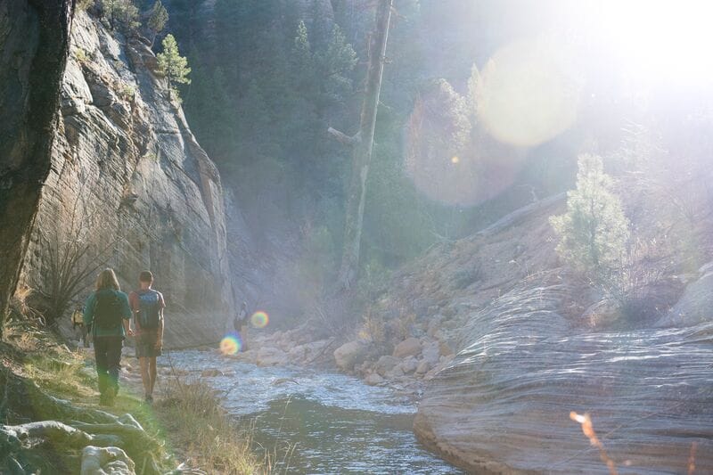 Two people walking along a stream in a canyon.