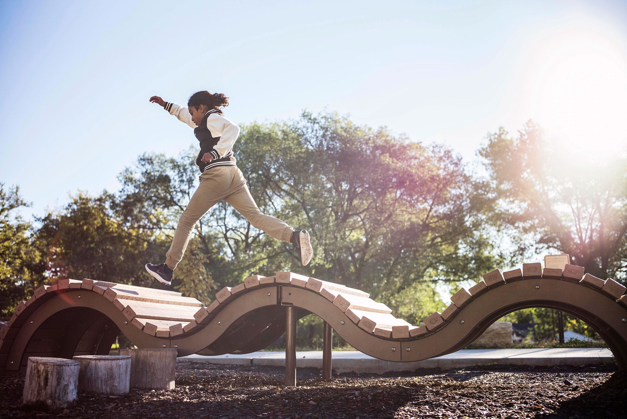 A boy jumping on a wooden structure in a park.