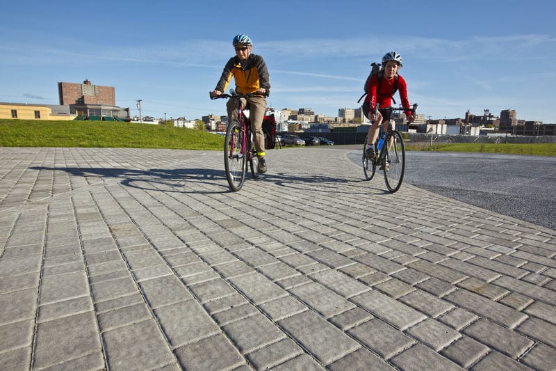 Two people riding bicycles on a brick path.