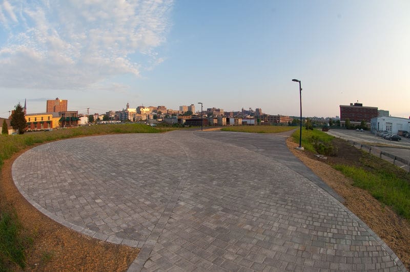 A view of a brick paved parking lot with a city in the background.