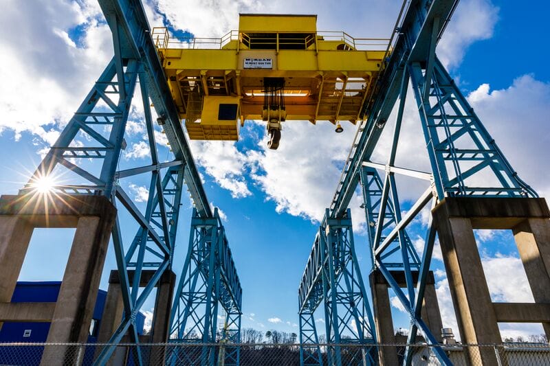 A yellow crane lifts a blue crane over a blue sky.
