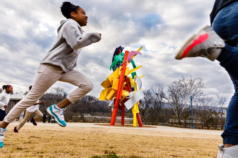 A group of children running in front of a colorful sculpture.