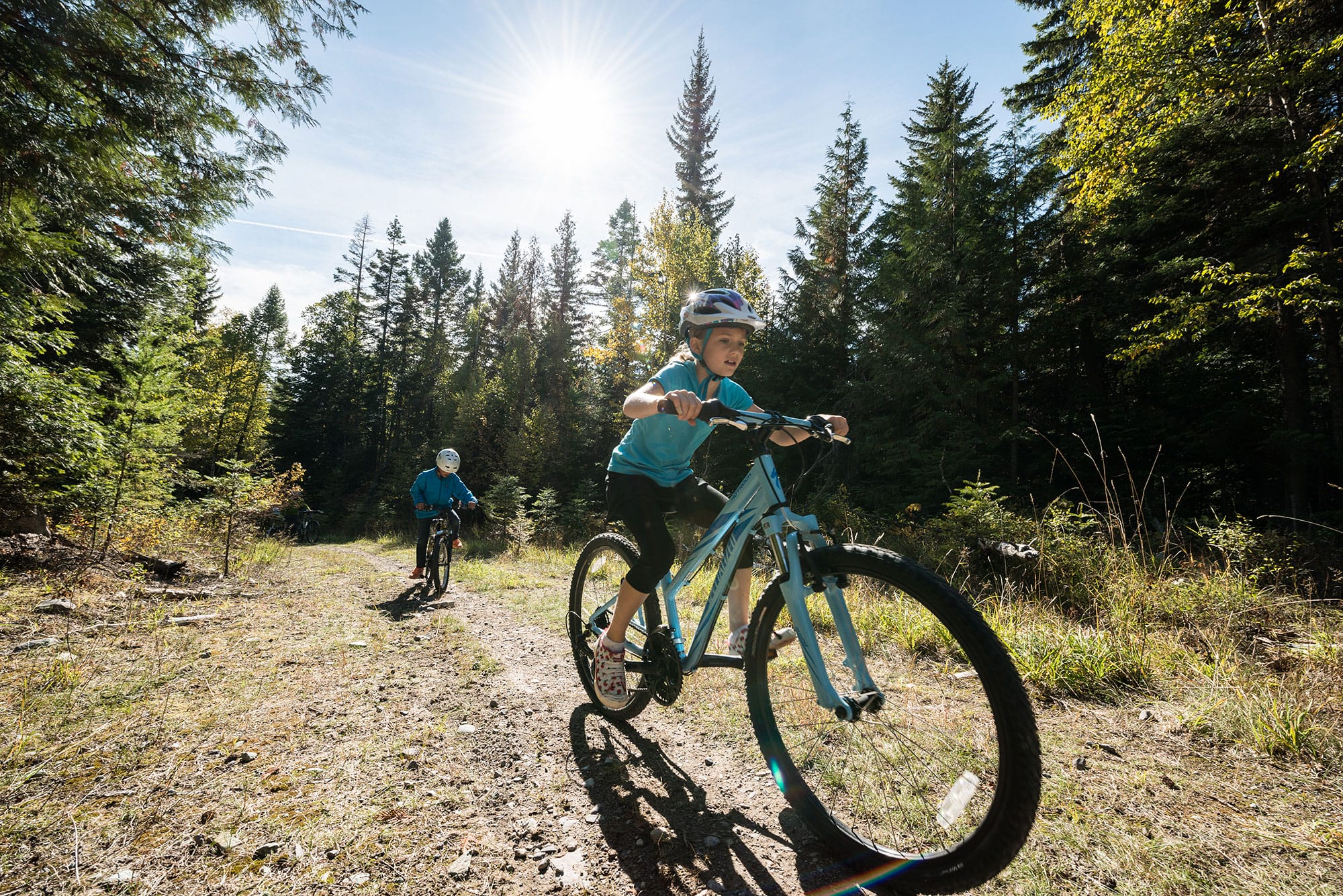 A boy riding a blue mountain bike in the woods.