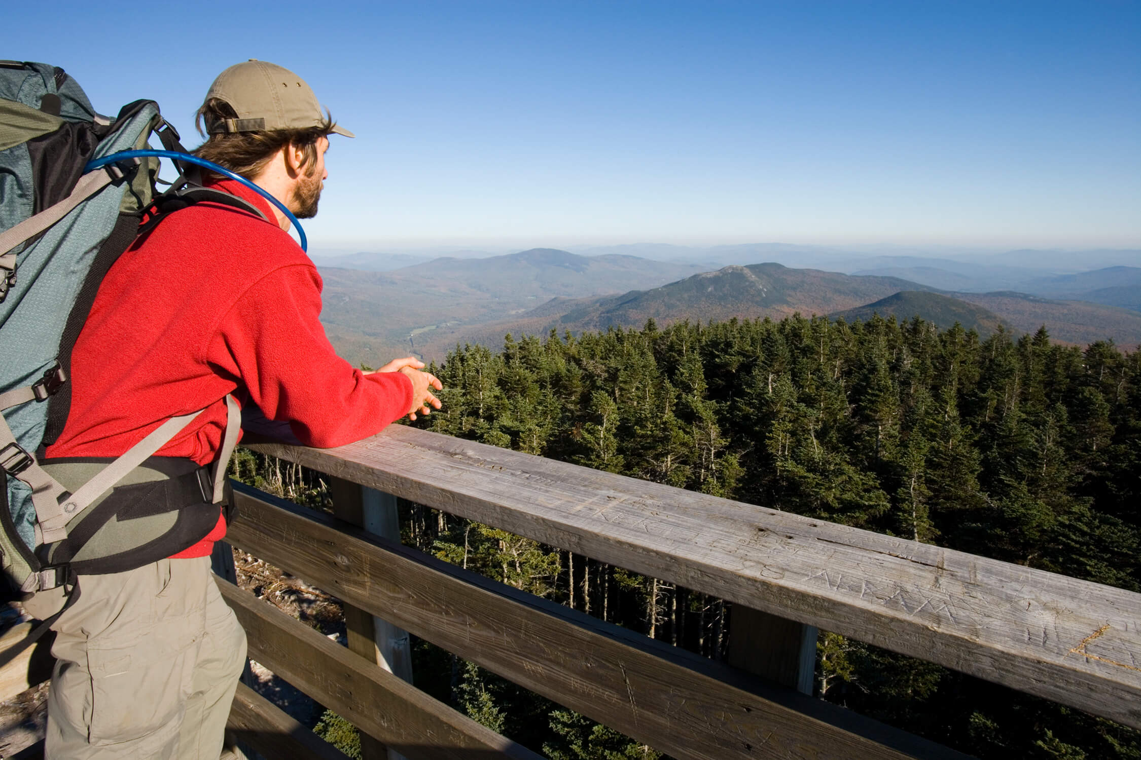 A man with a backpack on a railing overlooking a mountain.