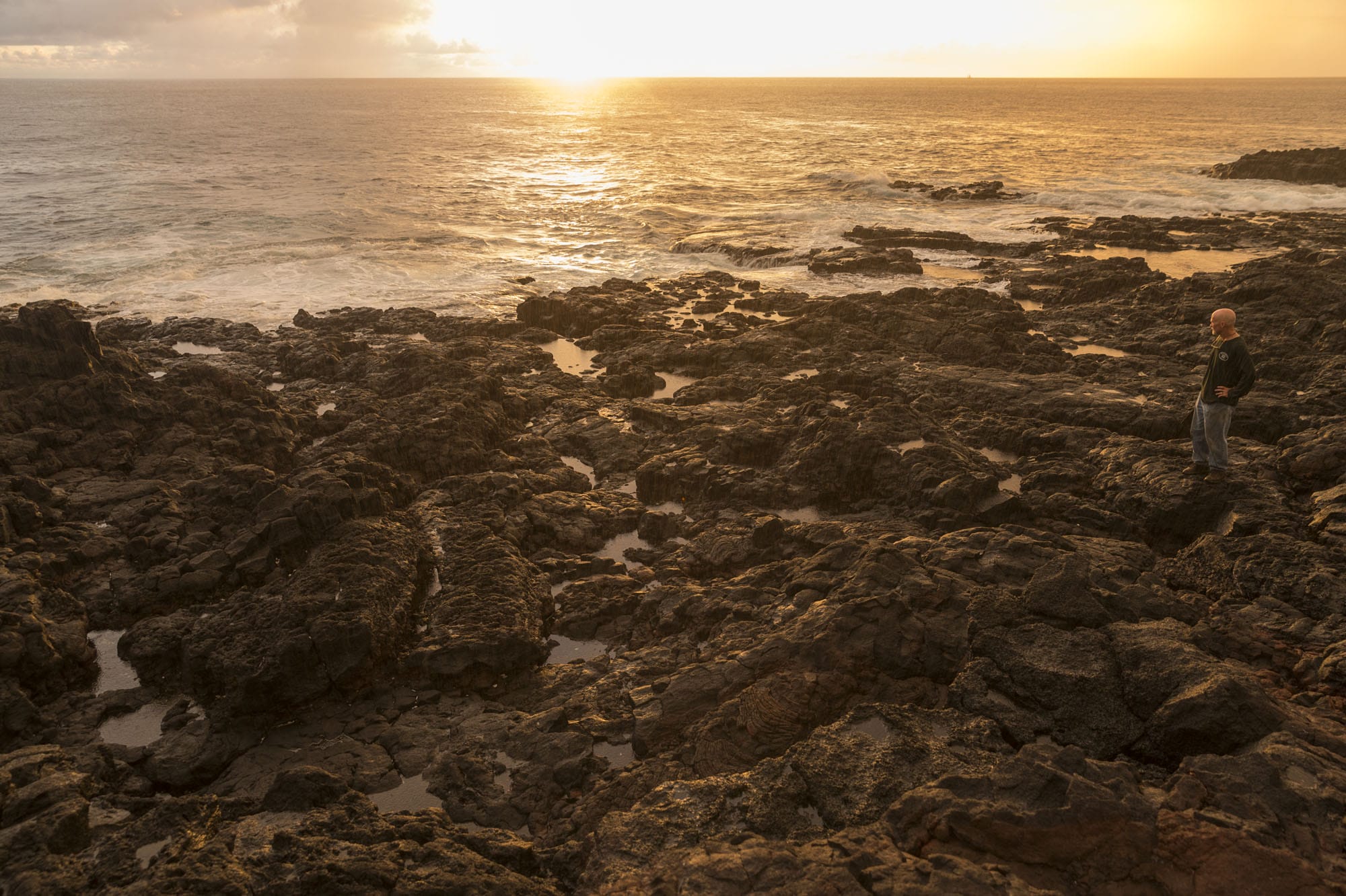 A man standing on a rocky beach at sunset.