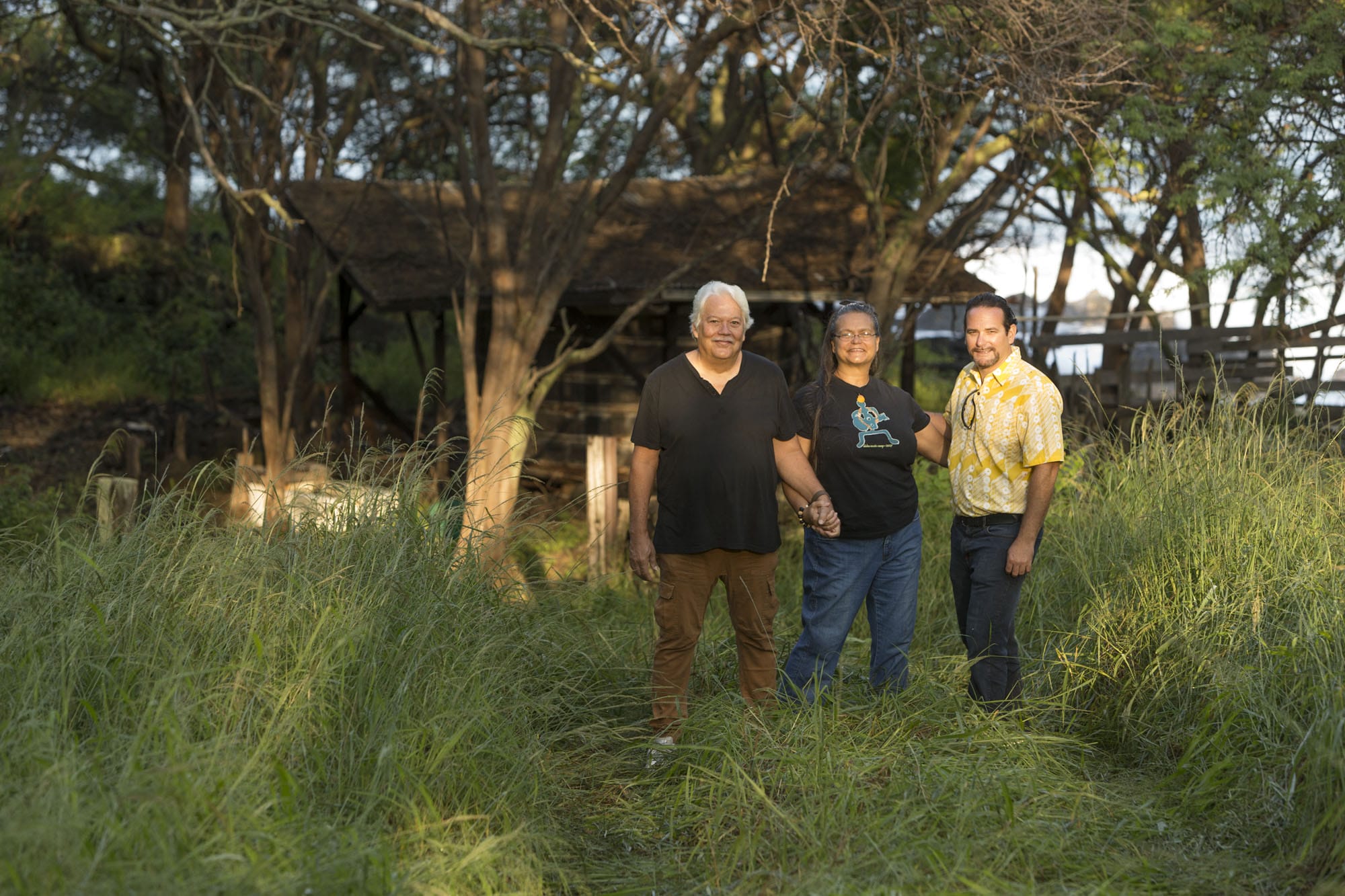 Three men standing in tall grass next to a shack.