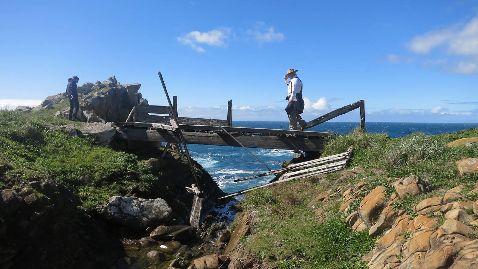 Two men standing on a wooden bridge near the ocean.