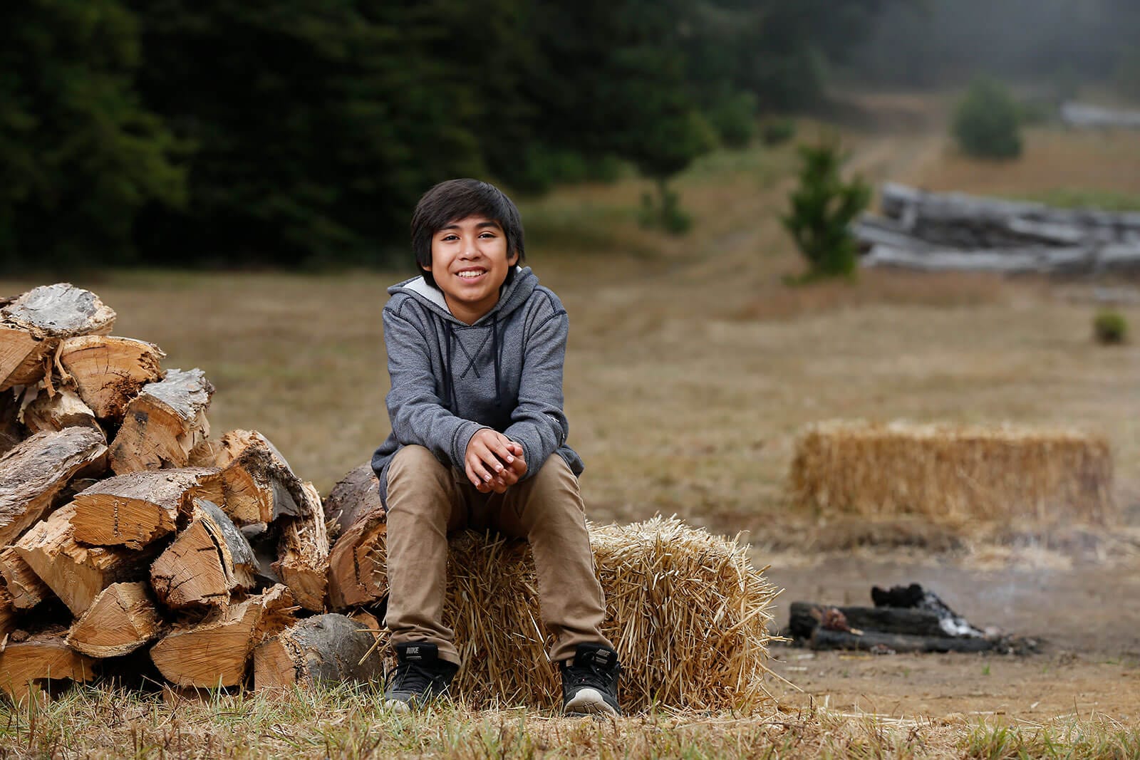 A young man sitting in front of a pile of hay.