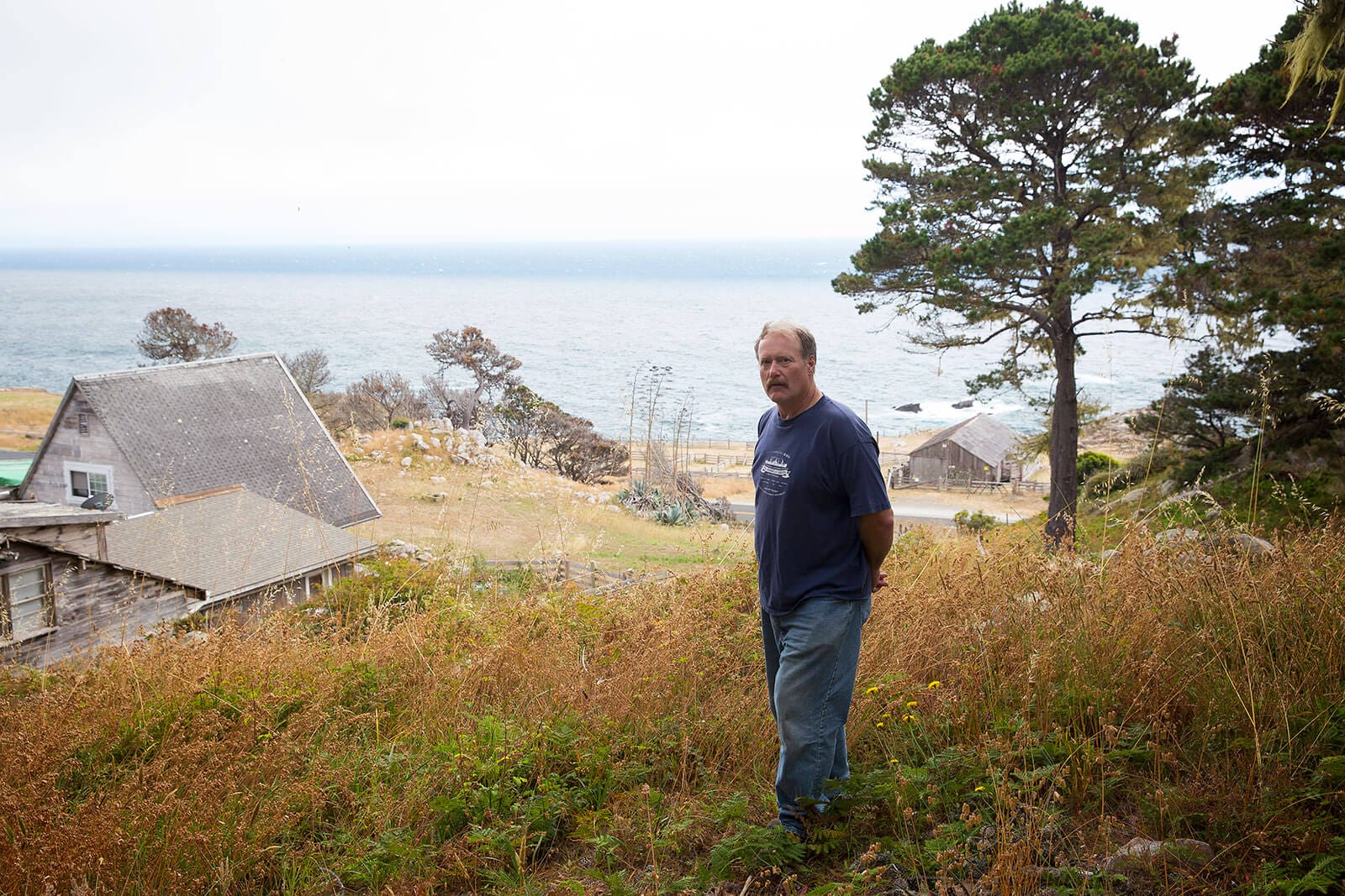 A man standing in a grassy area near the ocean.