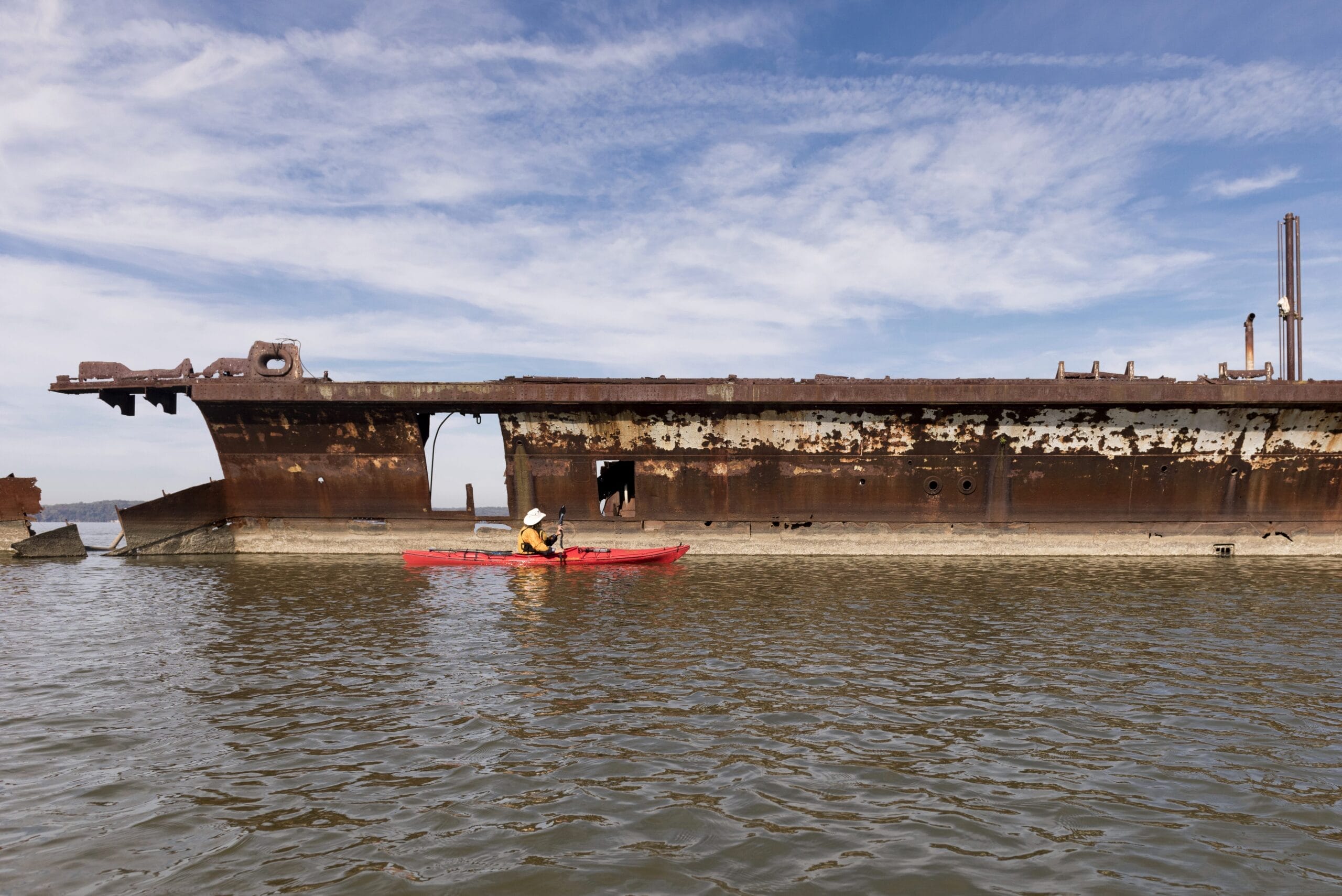 A person in an orange kayak paddles around a large shipwreck.