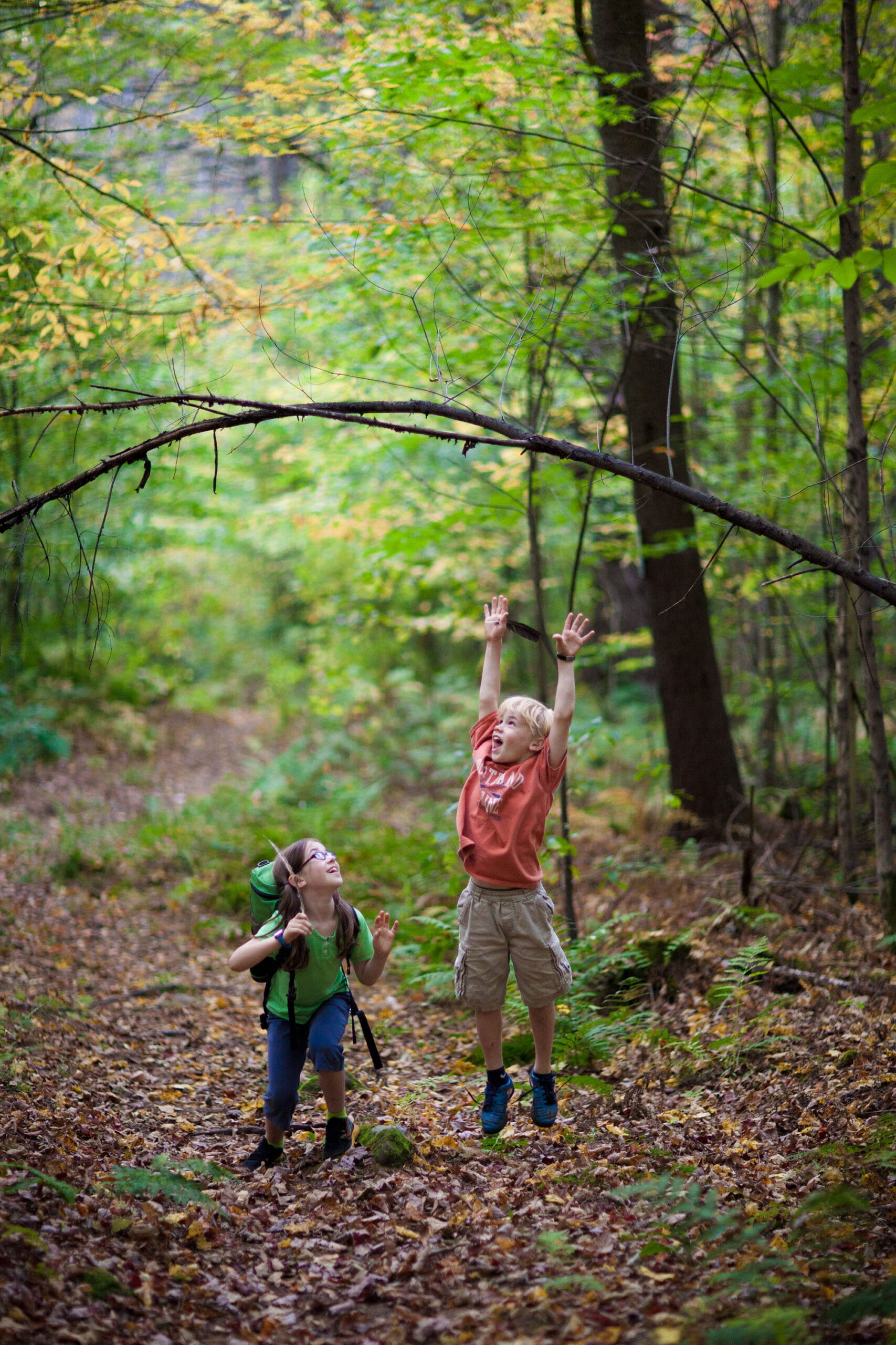 Two children are playing in a wooded area.