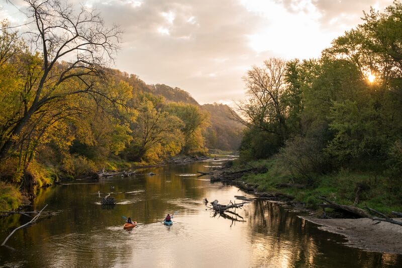 A group of people canoeing down a river with trees in the background.