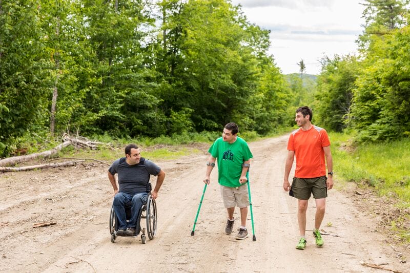 Three men in wheelchairs walking down a dirt road.