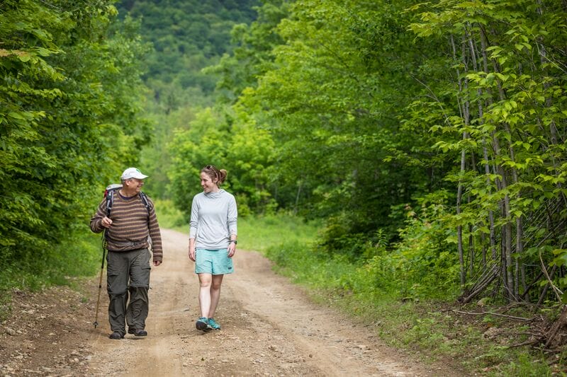 A man and woman walking down a dirt road in the woods.