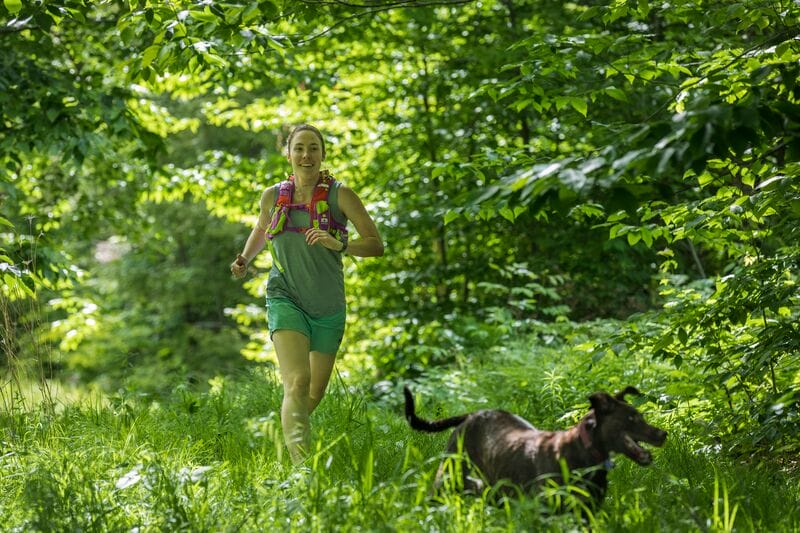 A woman jogging with her dog in the woods.