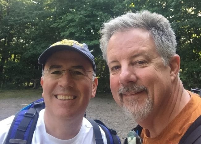 Two men smile for a selfie in a forest