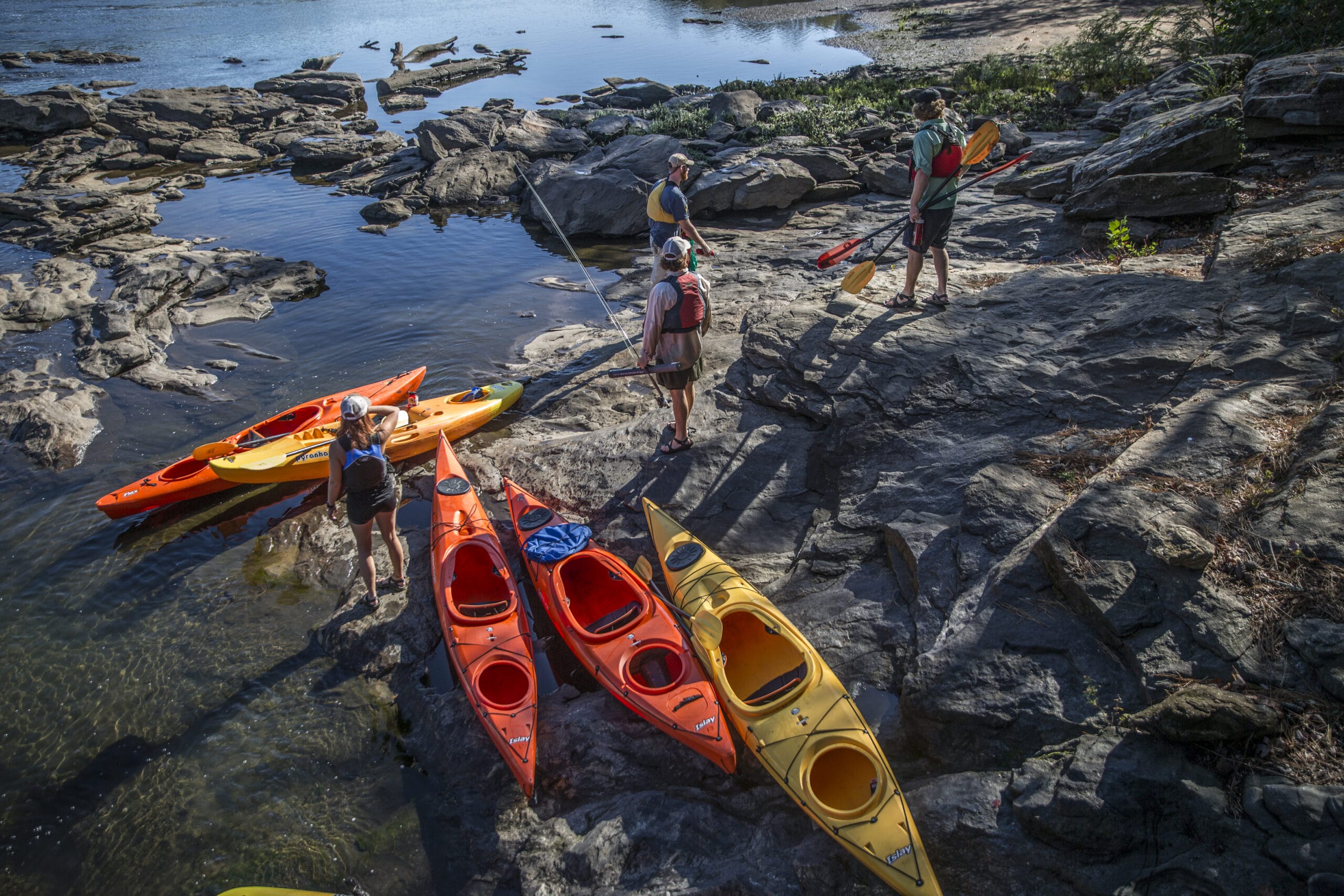 A group of people standing next to a group of kayaks.