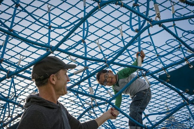 A boy in glasses climbs in a net 