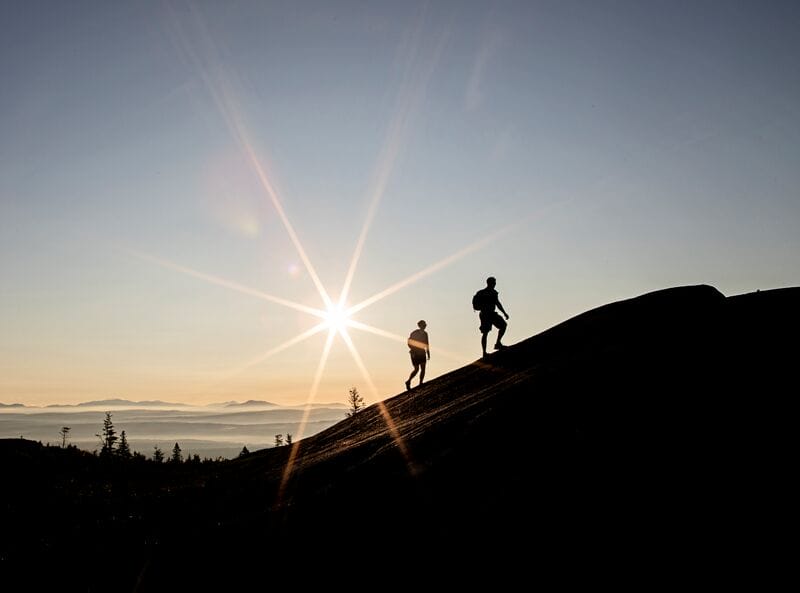Two people walking on a mountain at sunset.