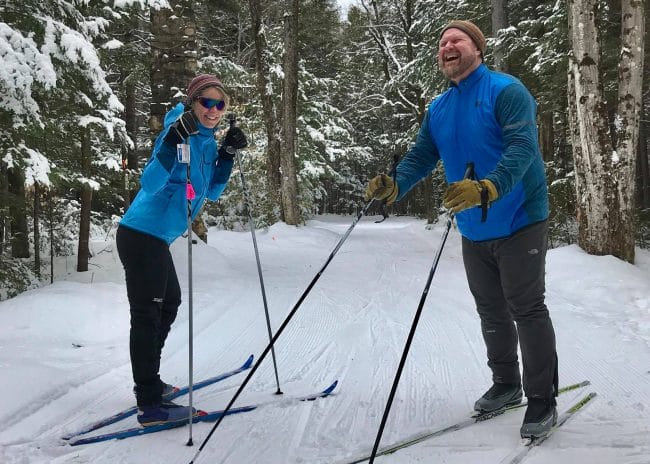 A man and a woman on cross country skis in a forest