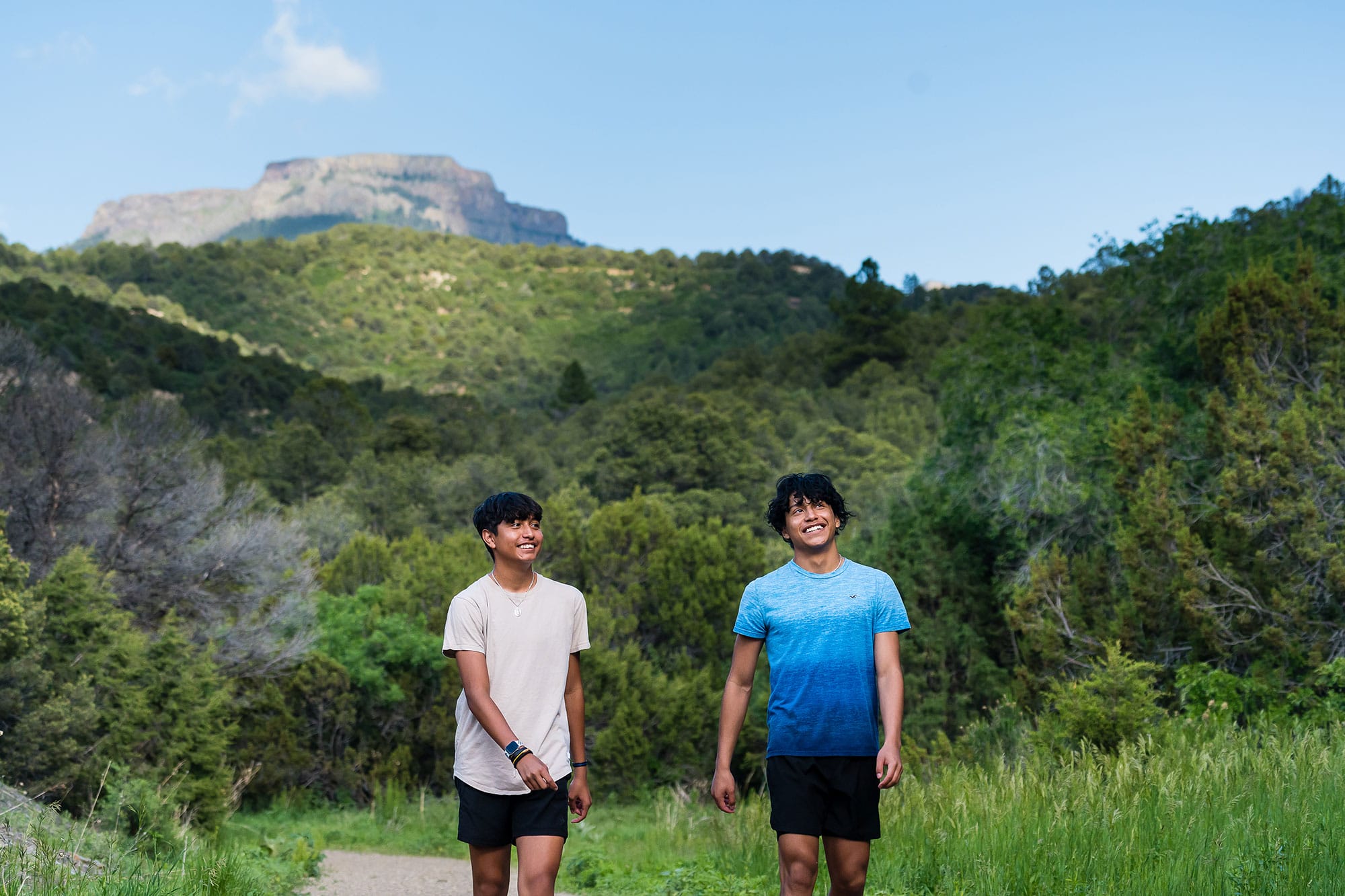 Two young men walking on a trail with mountains in the background.