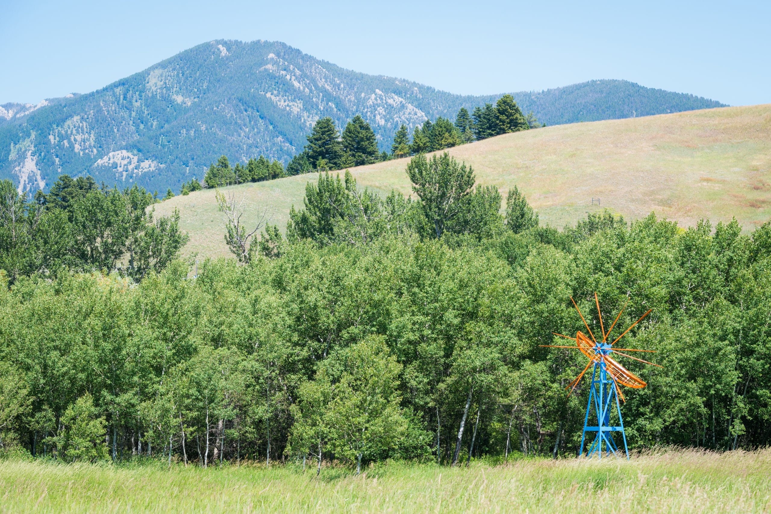 A windmill sculpture in front of trees and mountains