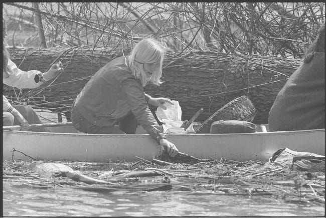 A girl in a canoe picking trash out of a river in 1970