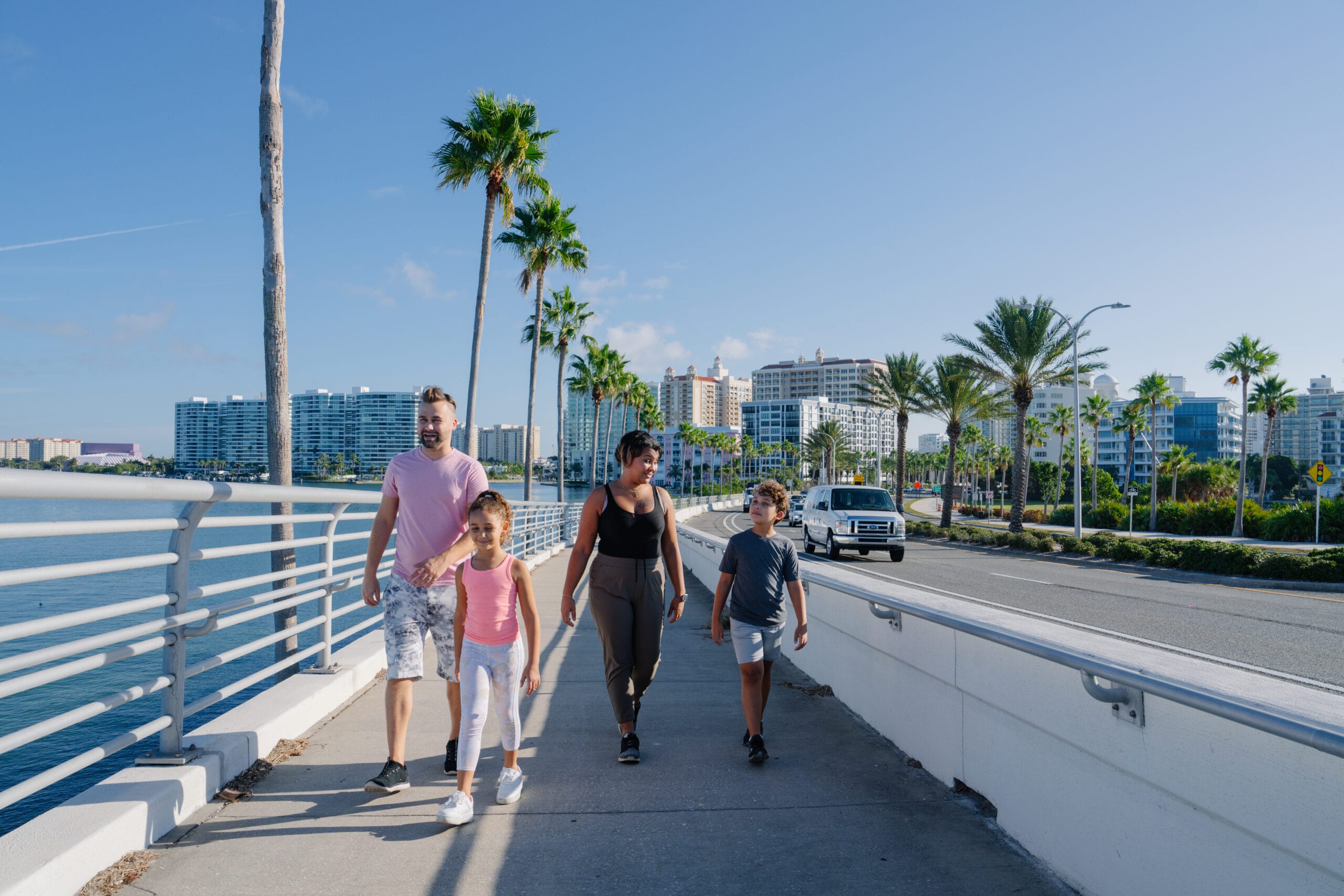 A family walks along a boardwalk with palm trees in the background.
