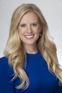 A blonde woman in a blue dress smiling.