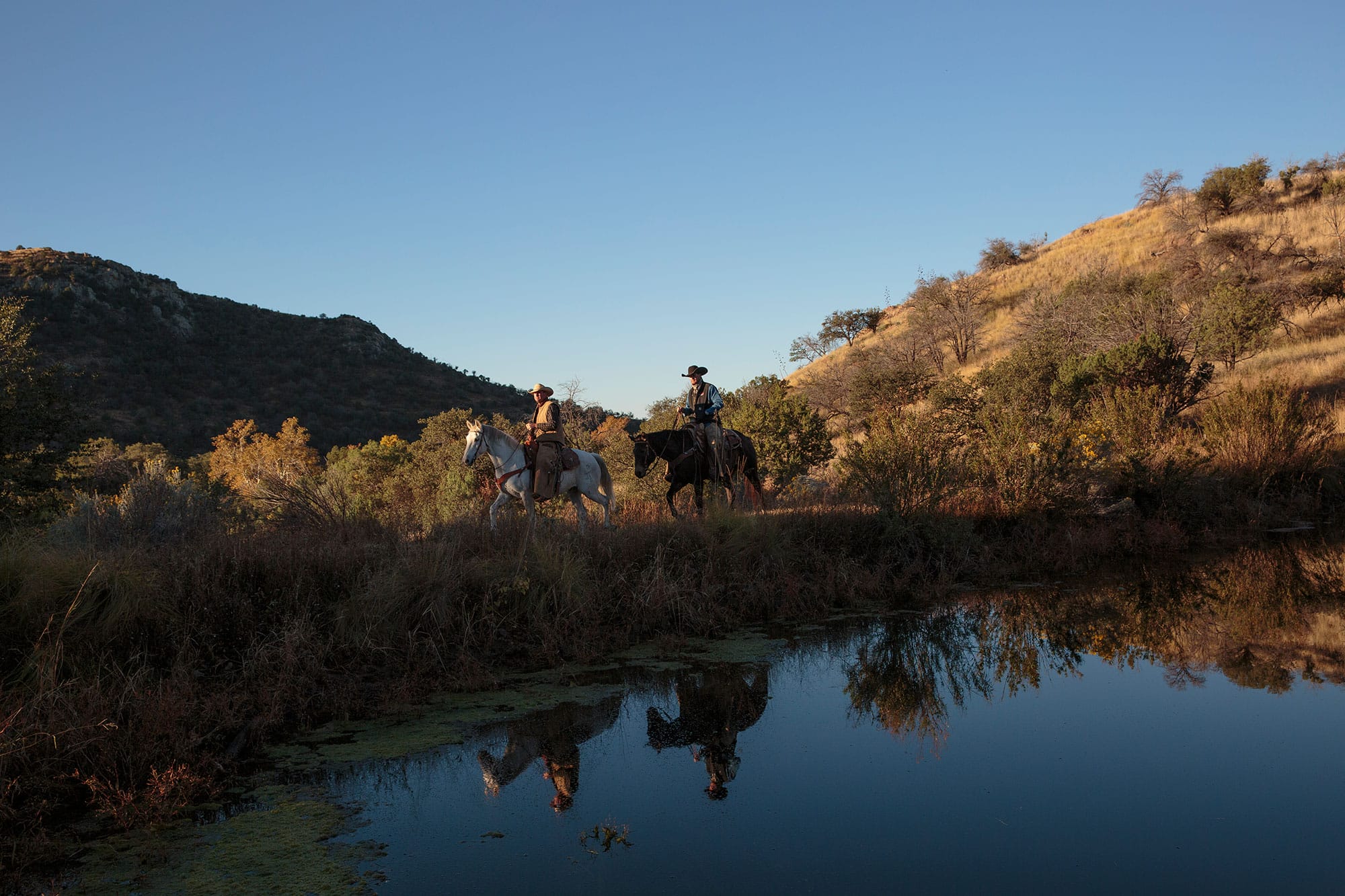 Two people riding horses near a pond.