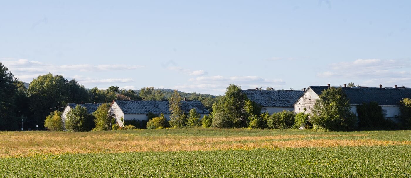 A group of buildings in a field with trees in the background.