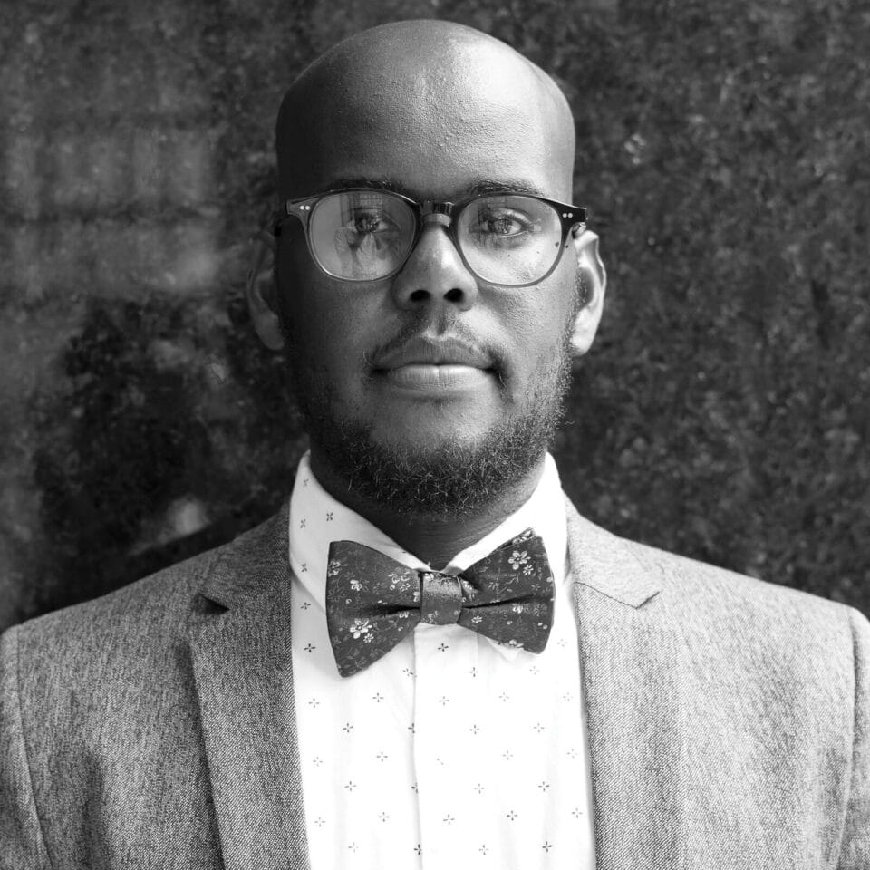 A black and white photo of a man wearing glasses and a bow tie.