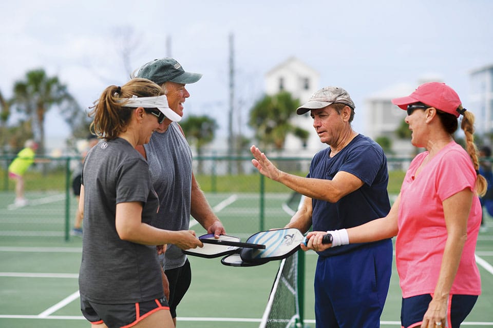 A group of people talking to each other on a tennis court.