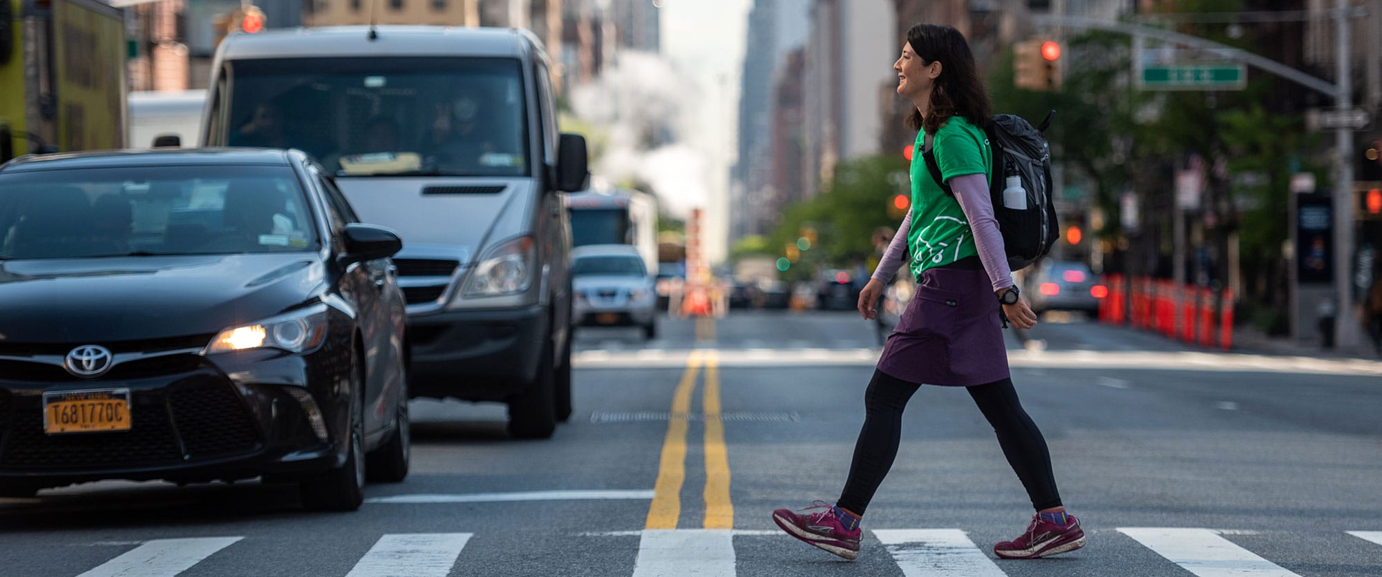 A woman is crossing the street in front of a car.