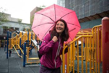A woman holding a pink umbrella in front of a playground.