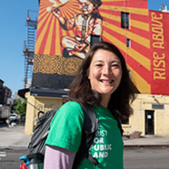 A woman in a green shirt standing in front of a mural.