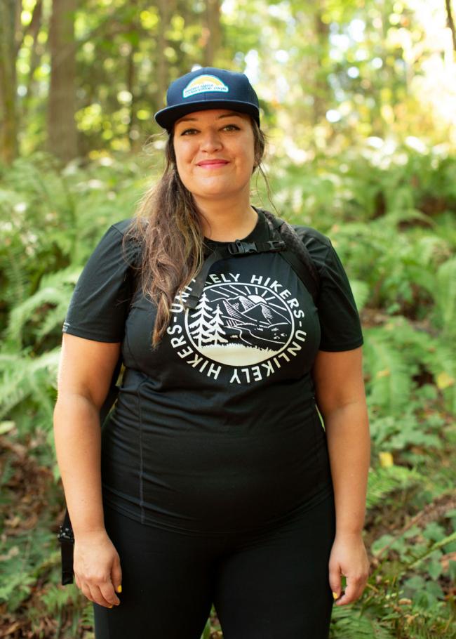 A woman standing in the woods wearing a black t - shirt.