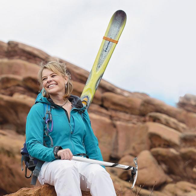 A woman sitting on a rock holding her skis.
