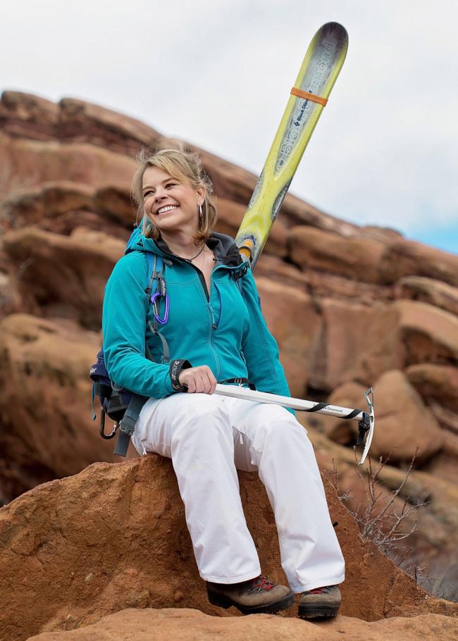 A woman sitting on top of a rock holding skis.