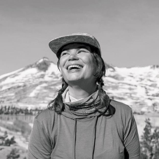 A black and white photo of a woman smiling in front of mountains.