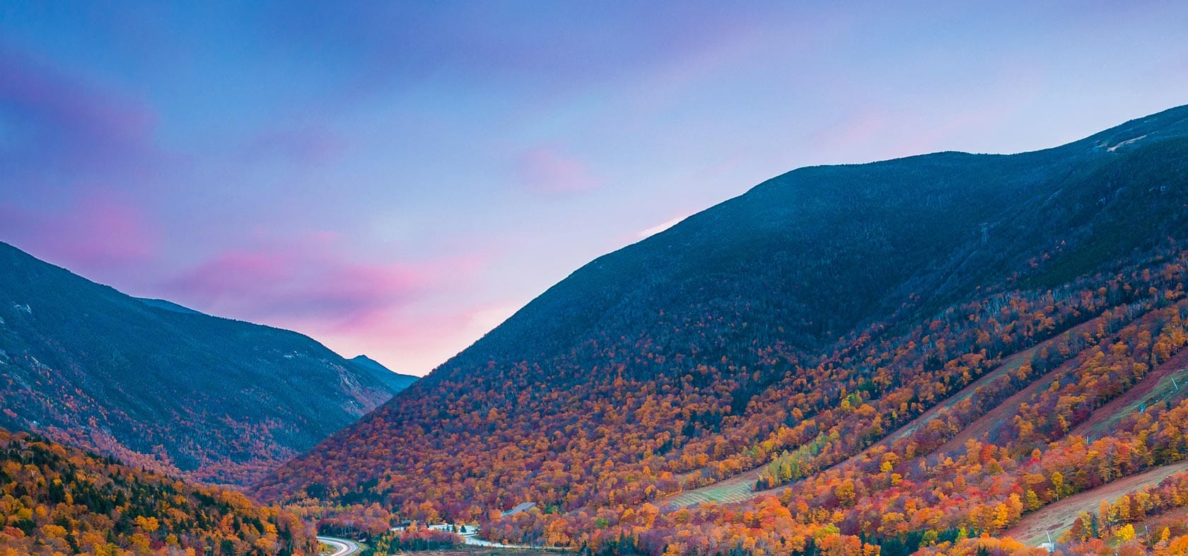 A valley with colorful trees and a river in the background.