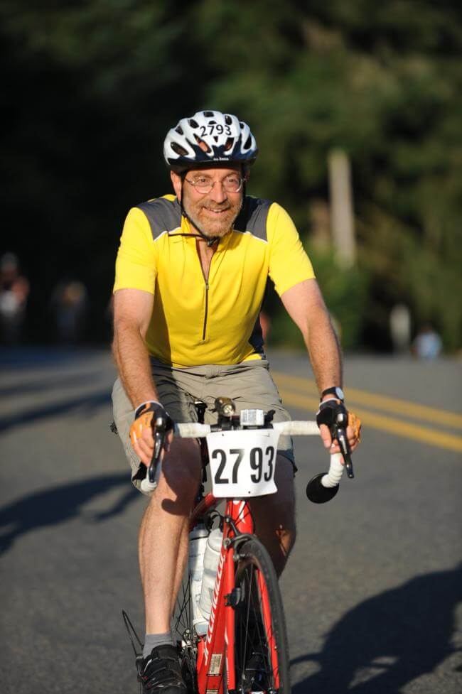 Wearing a yellow and gray jersey, Dr. Howard Frumkin rides a red bike in the the classic STP (Seattle to Portland) bike ride.