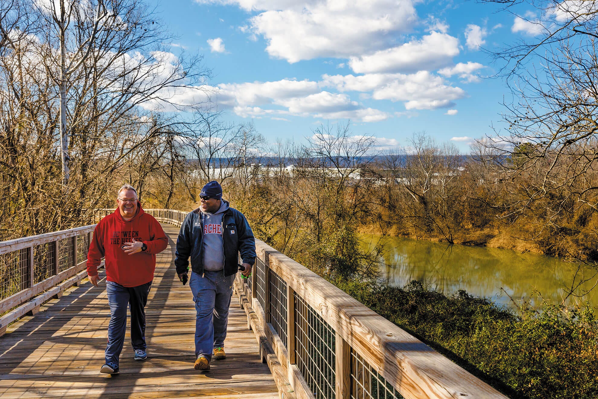 Two men walking on a wooden bridge.